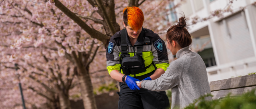 Amber Velay-Mah, Patrol Officer providing first aid in front of a row of cherry blossom trees